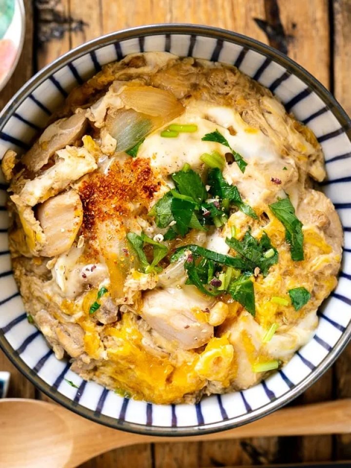 A bowl of oyakodon with soft egg and chicken over rice, topped with spring onion