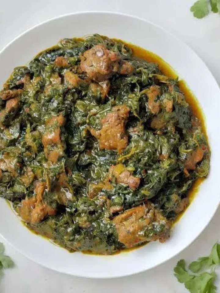 A pot of dark green Palak Gosht with pieces of mutton, topped with ginger matchsticks, served with roti and lemon wedges