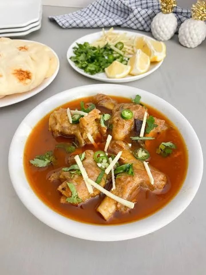 Bowl of Pakistani paya with tender trotters in a glossy spiced gravy, garnished with ginger, green chillies and coriander, served with naan and lemon.