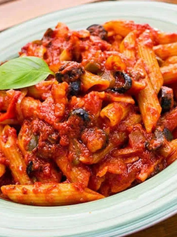 A bowl of penne arrabbiata in a glossy red chilli tomato sauce topped with parsley and cheese