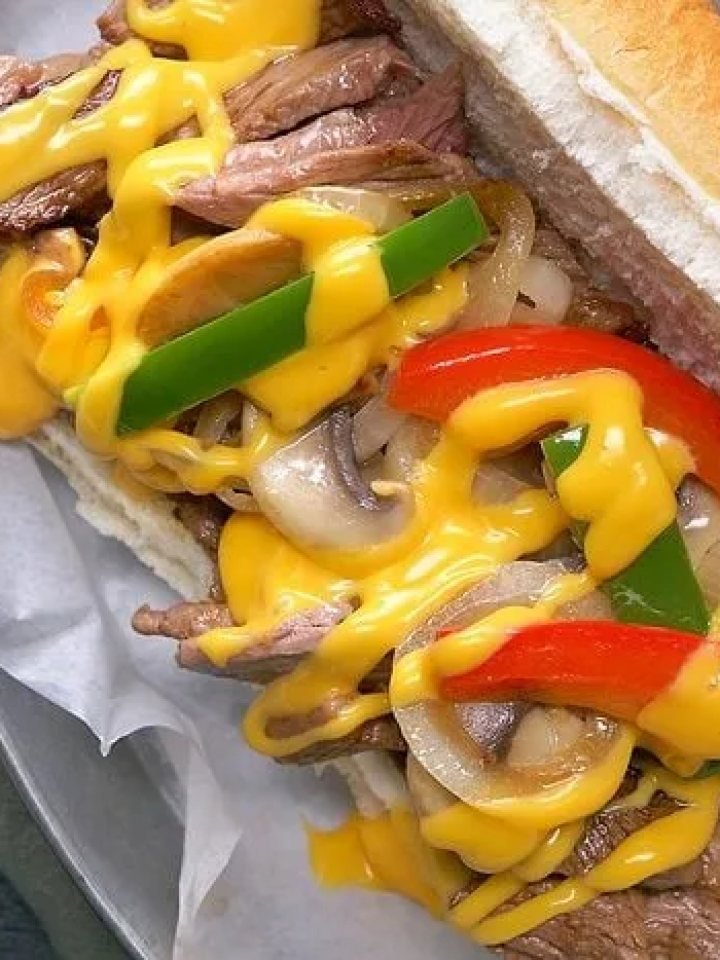 Two Philly cheesesteak sandwiches filled with sliced beef, onions and melted cheese on a wooden board