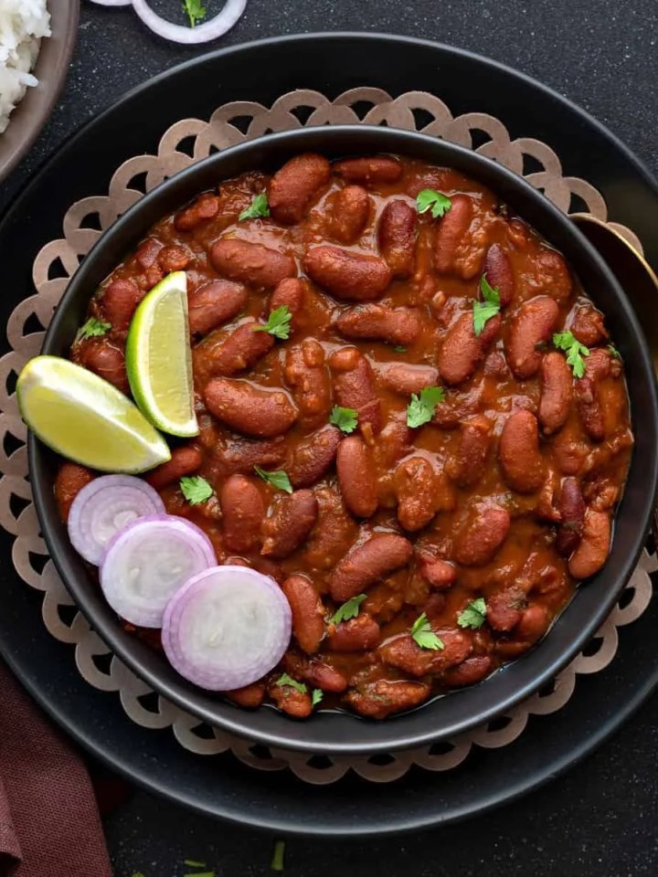 A bowl of rajma masala, red kidney beans in a thick spiced tomato gravy, served with basmati rice, onion and lemon.