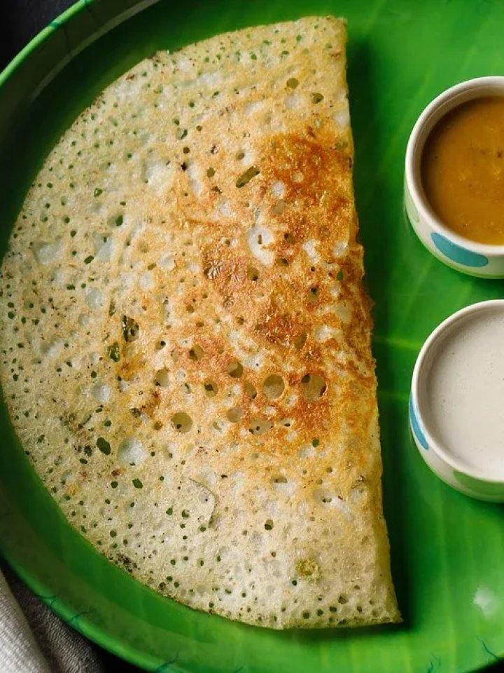 Crisp golden lacy rava dosa folded on a plate with coconut chutney, tomato chutney and sambar