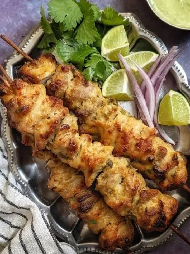 Golden grilled reshmi chicken kababs on skewers with mint chutney, onion rings, lemon and naan