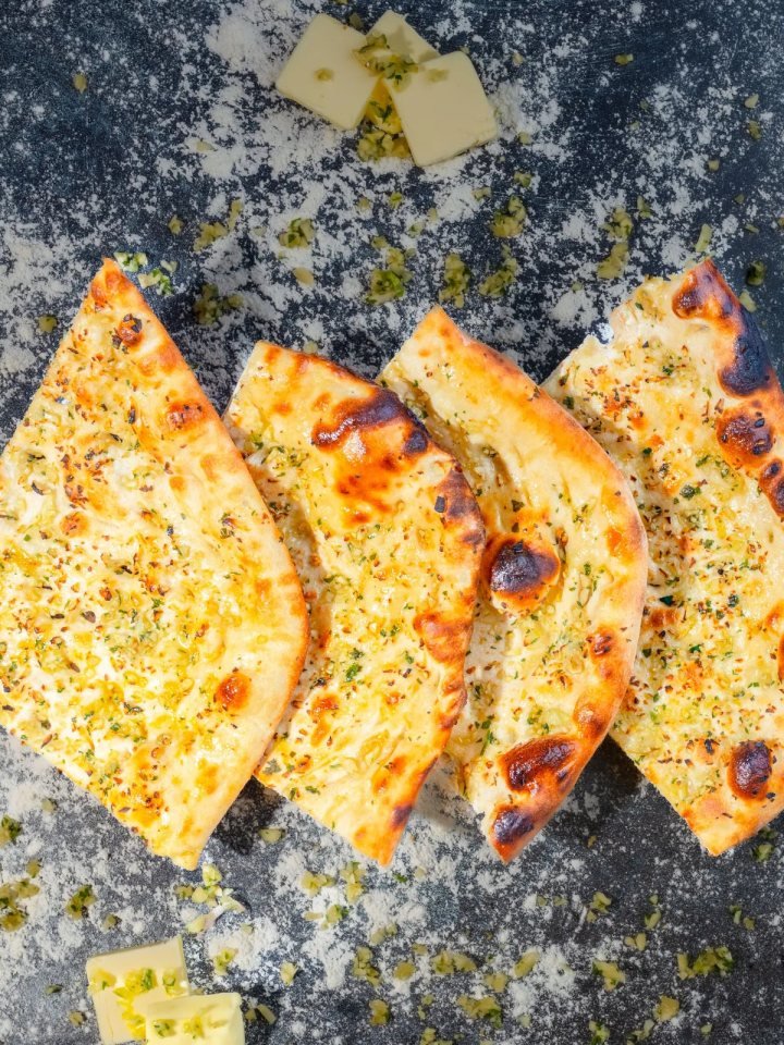 Freshly baked roghni naan topped with sesame and nigella seeds on a wooden board