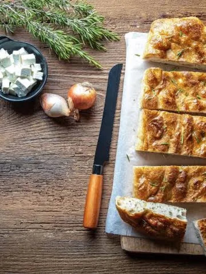 Golden rosemary focaccia in a baking tray with olive oil dimples, rosemary sprigs and coarse salt on top