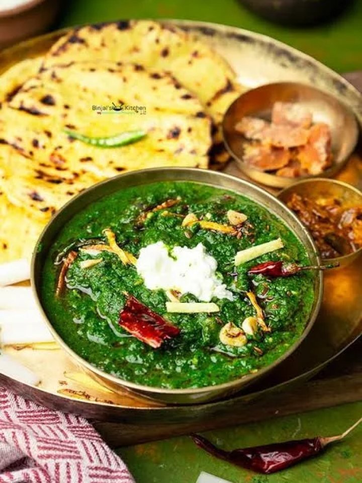 A bowl of thick green sarson ka saag topped with white butter and a ghee tarka, served with makki ki roti