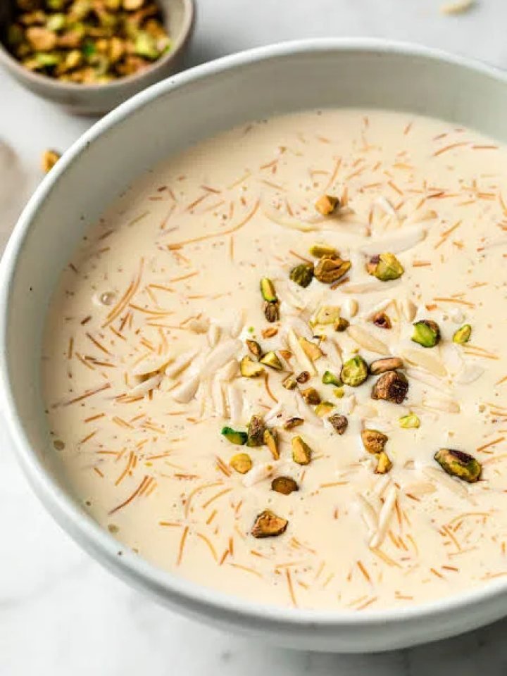 Bowl of sheer khurma with vermicelli, dates and sliced nuts, garnished with pistachios and saffron