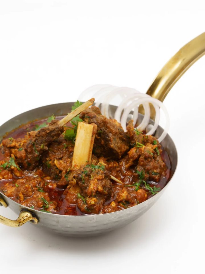 A karahi of glossy Shinwari lamb karahi topped with green chillies, ginger and coriander, served with naan and lemon.