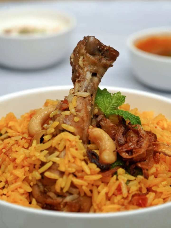 A pot of Sindhi biryani with saffron rice, potatoes, dried plums, green chillies and fresh herbs