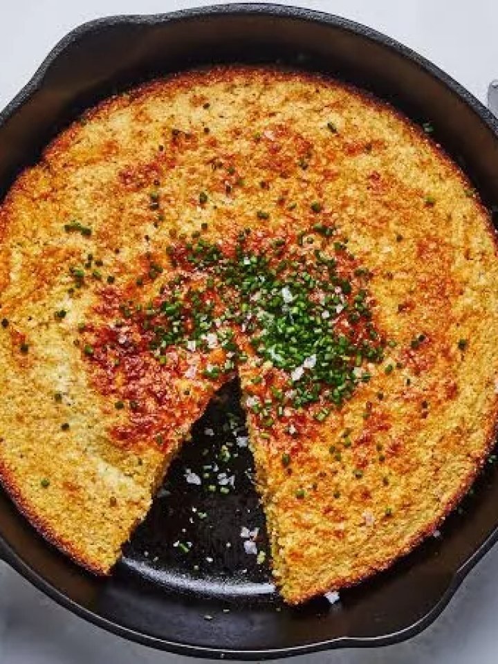 Golden skillet cornbread in a cast iron pan with one wedge cut and a pat of melting butter on top