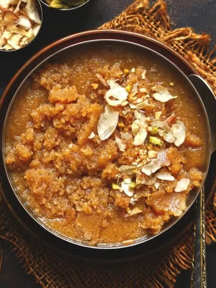 Golden semolina halwa garnished with almonds and pistachios in a small brass pan