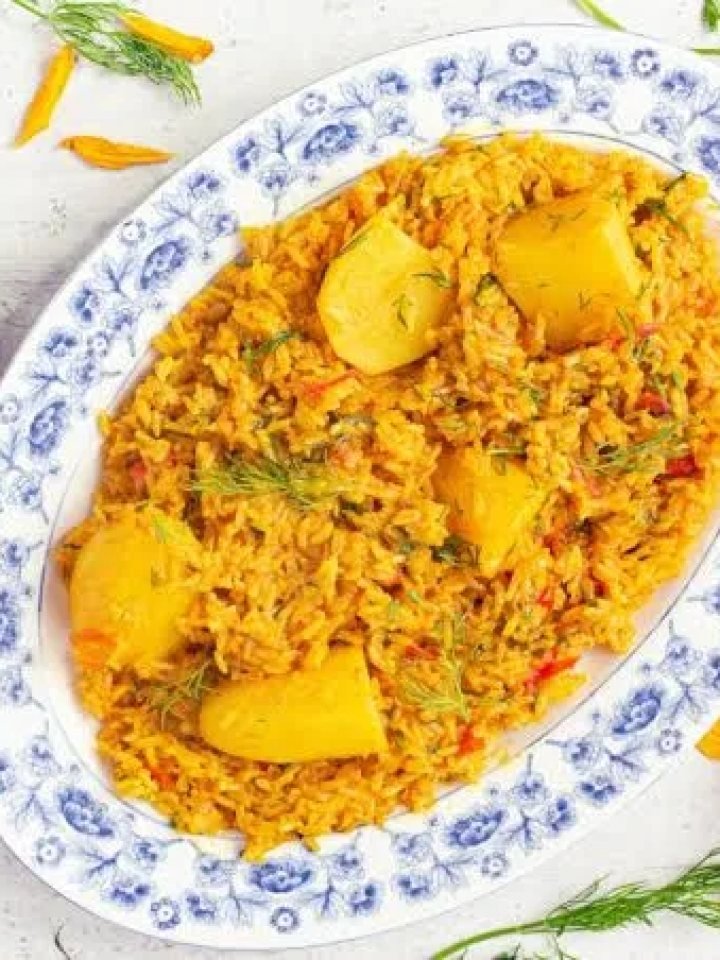 A pot of golden tahiri rice with potatoes and green peas, garnished with fresh coriander and mint