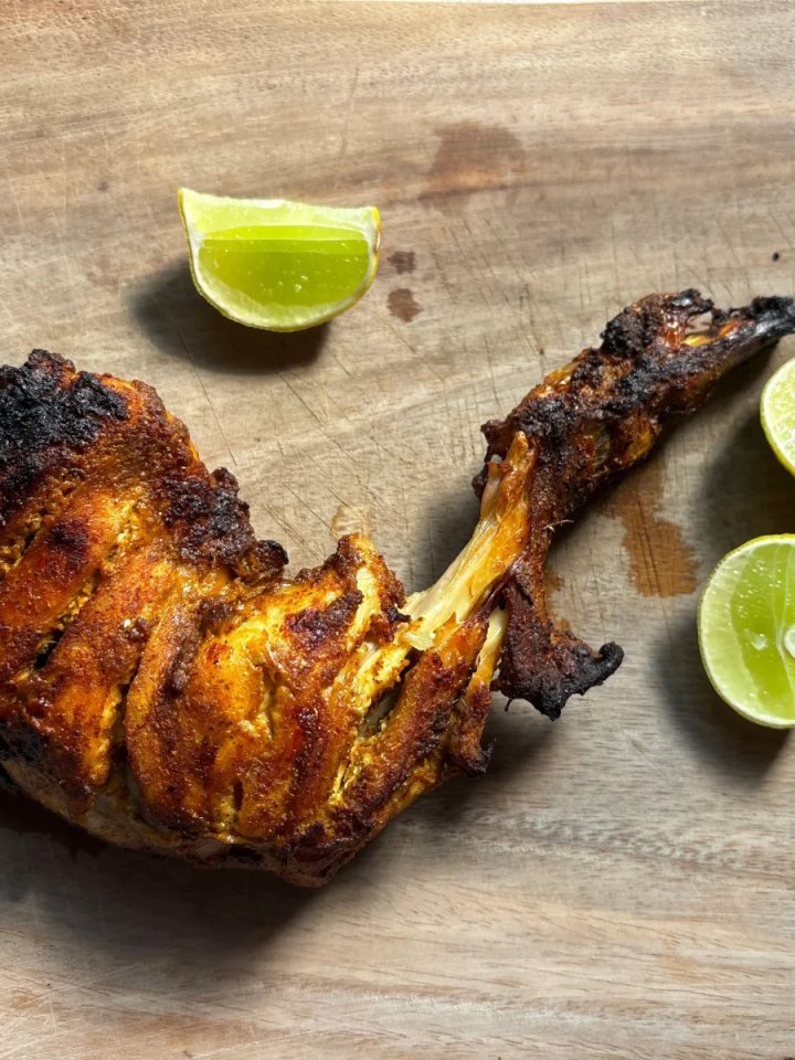 Charred red tandoori chicken legs served with onion rings, lemon wedges and green chutney