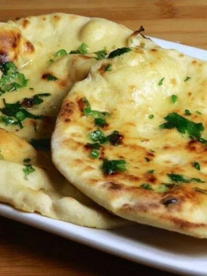 Stack of freshly cooked butter-brushed naan topped with nigella and sesame seeds on a wooden board