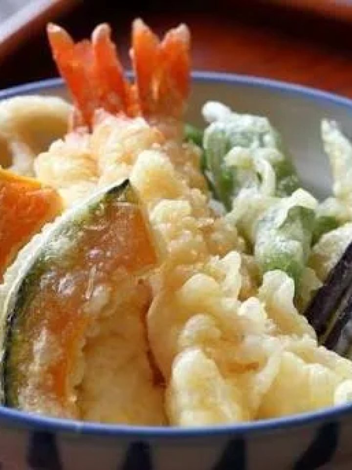 Bowl of rice topped with golden prawn and vegetable tempura glazed with soy sauce and garnished with spring onion