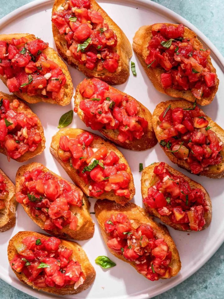Toasted bread slices topped with diced tomatoes and fresh basil on a wooden board