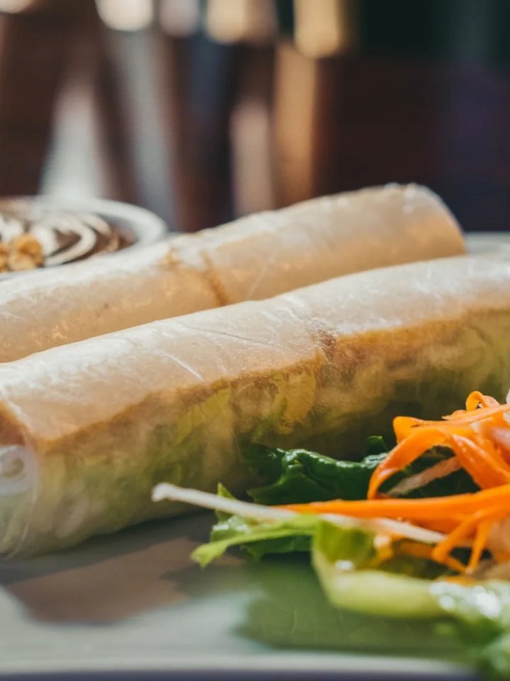 Golden fried vegetable spring rolls on a plate, one cut open to show cabbage and carrot filling, with chilli sauce