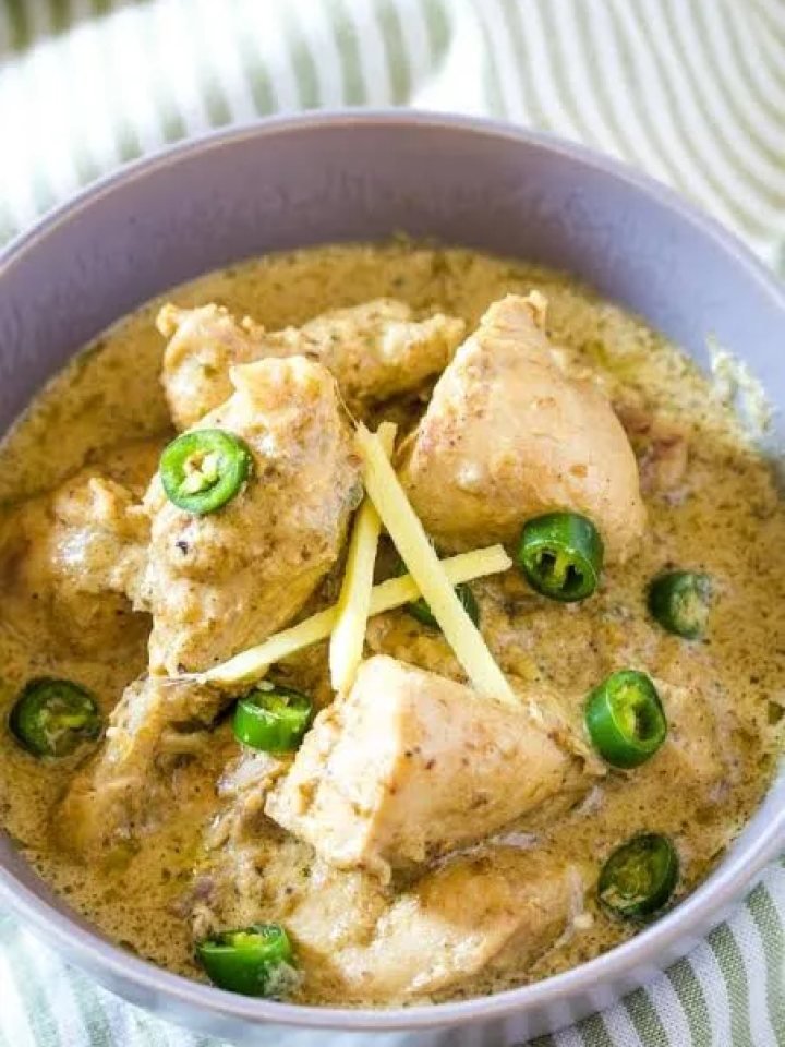 A karahi of creamy white chicken curry garnished with ginger strips, green chillies and fresh coriander, served with naan
