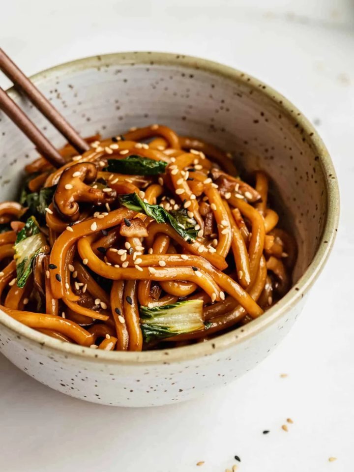 A bowl of yaki udon with chicken, cabbage and carrot, topped with spring onion and sesame seeds