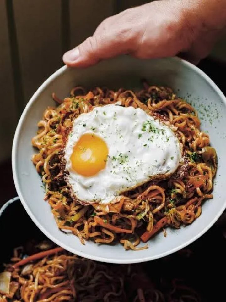 Plate of yakisoba noodles with chicken, cabbage and carrot, garnished with pickled ginger and spring onion