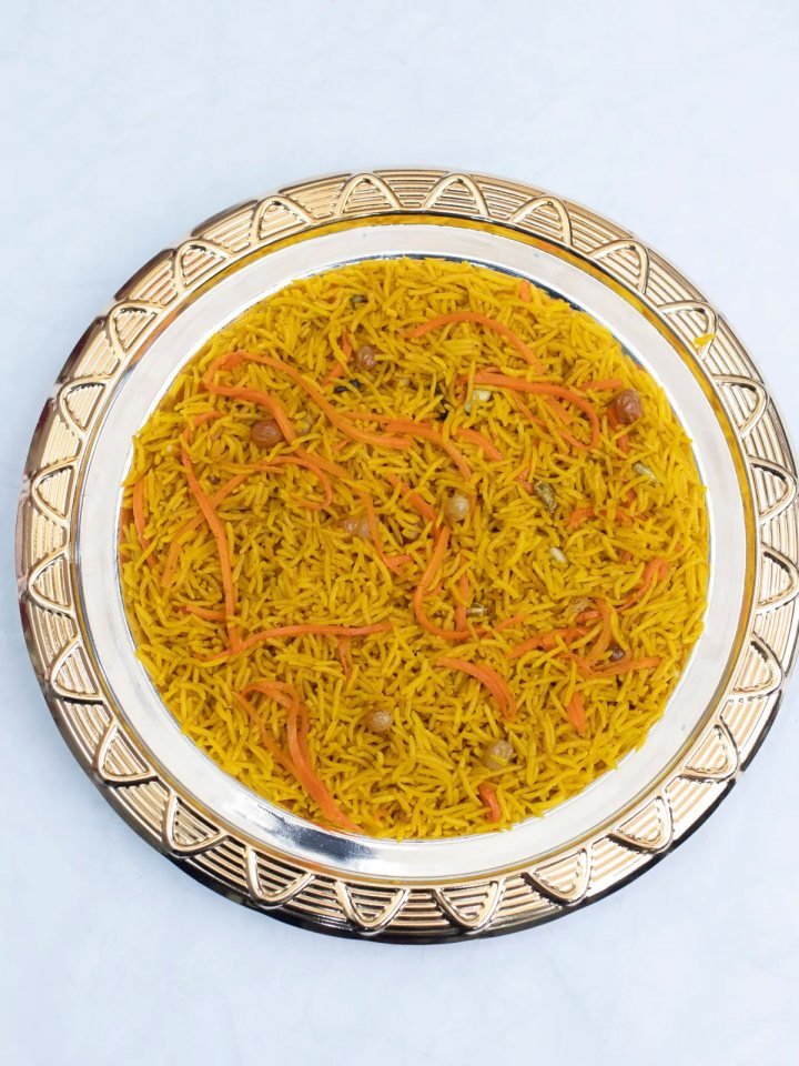 A serving dish of golden zarda sweet rice topped with sliced pistachios, almonds and raisins